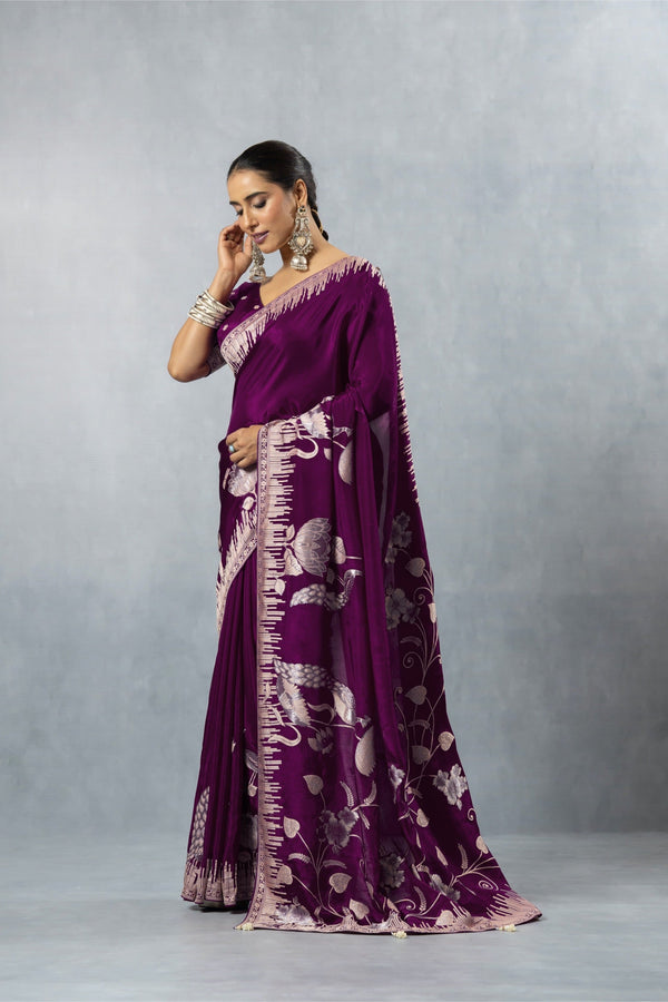 Side profile of a model showcasing the full drape and fluid fall of the Vanya plum purple satin silk saree with its elaborate silver woven border.