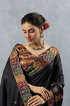 A close-up showing the rich, multi-color Patola-style printed border of the Vanya Sarees black designer saree.