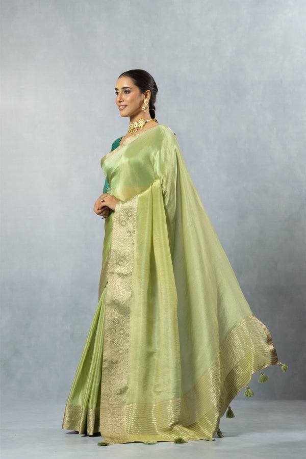 A beautiful side profile of the model wearing the Vanya Sarees green tissue silk saree, showing its shimmering texture and graceful drape.
