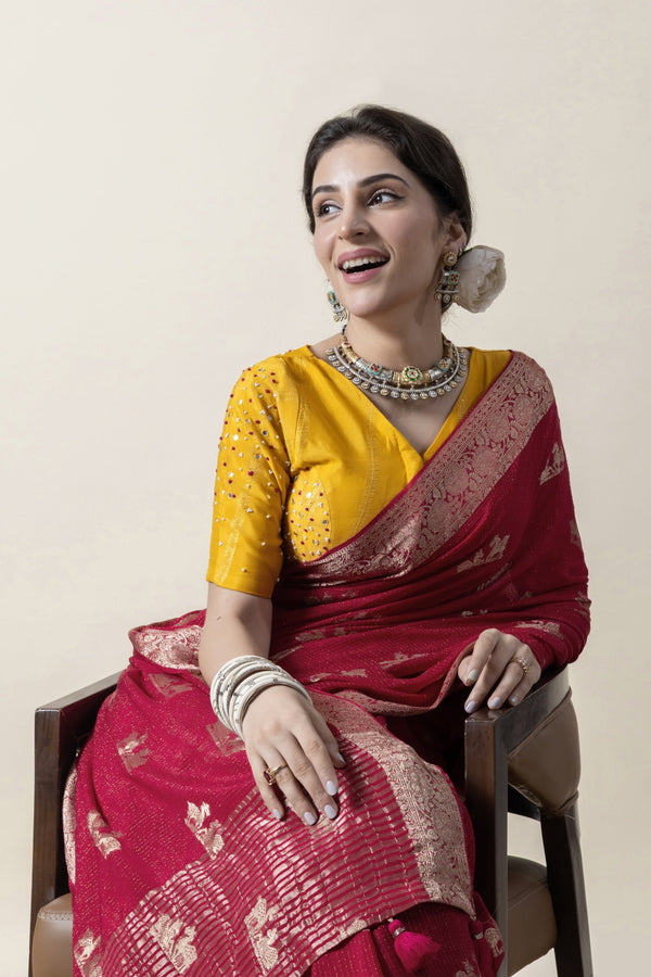 A smiling model seated gracefully in a Vanya Sarees maroon georgette saree, showcasing the hand-embellished yellow designer blouse.