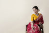 An elegant seated shot of the model in the Vanya Sarees maroon woven georgette saree, looking down gracefully.