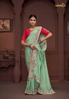 A full-length view of the model in Vanya Sarees' magnificent mint green saree with a heavy, multi-color embroidered border and red blouse.