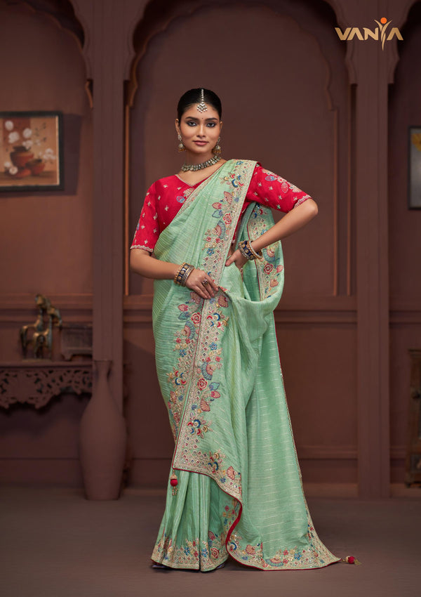 A full-length view of the model in Vanya Sarees' magnificent mint green saree with a heavy, multi-color embroidered border and red blouse.