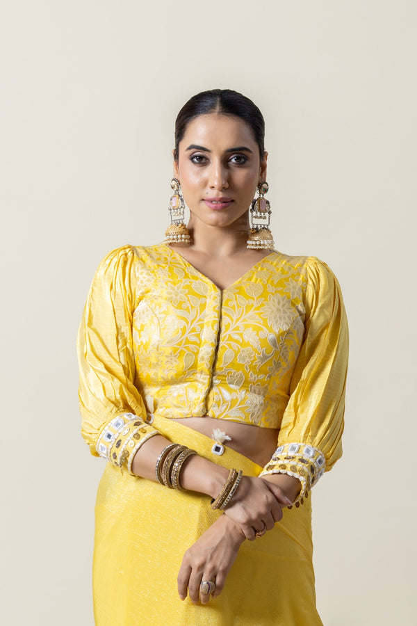 A clear front view of the Vanya Sarees readymade yellow brocade blouse, showing the V-neck, puff sleeves, and mirror work cuffs.