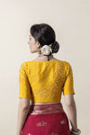 The back of the yellow designer blouse from Vanya Sarees, showcasing the sparkling hand-scattered crystal embellishments on the shoulders and sleeves.