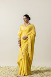 An elegant pose of the model in the Vanya Sarees yellow saree, showing the full length of the unique bow-detailed border.
