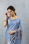 A close-up of the model in a Vanya Sarees blue linen saree, highlighting the artistic floral print with embroidery on the pallu.