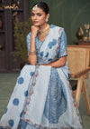 A beautiful seated portrait of the model in a Vanya Sarees blue printed saree, highlighting the delicate embroidered border and designer blouse.