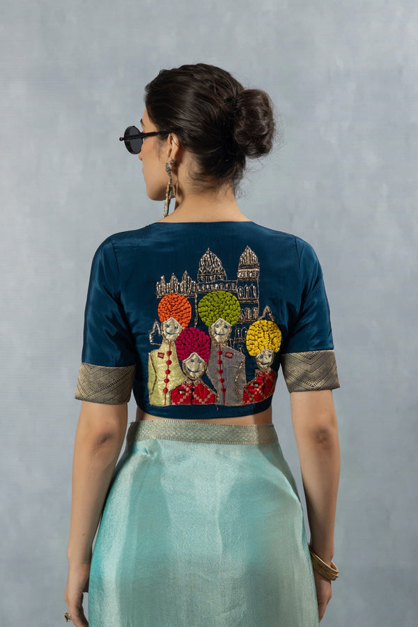 The unique, hand-embroidered 'Baraat' motif on the back of the teal blue designer blouse from Vanya Sarees, featuring men in colorful turbans.