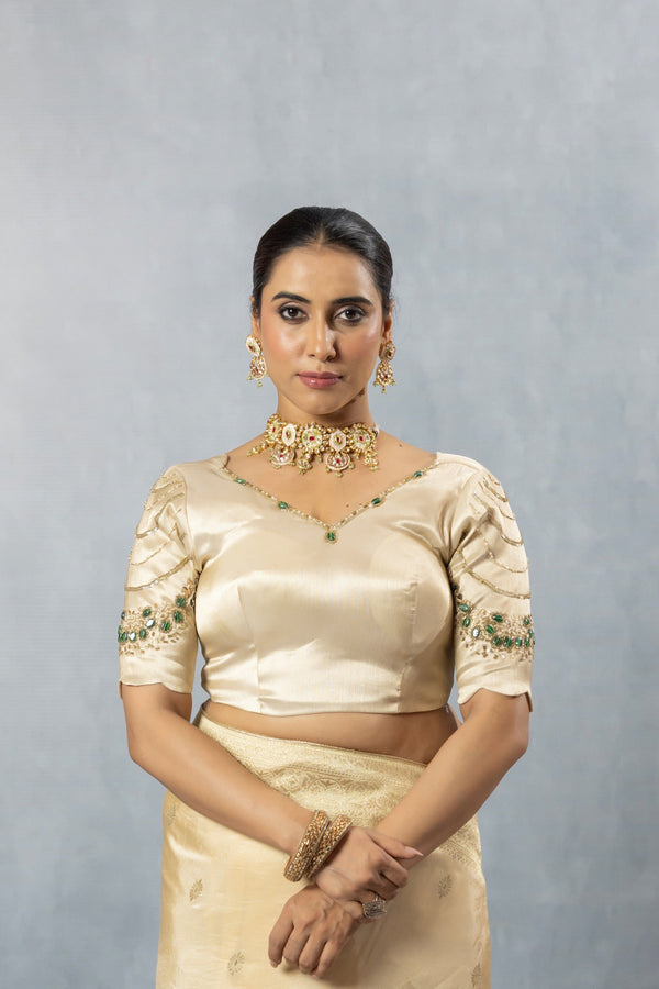 Close-up of Vanya's Champagne Gold Satin Silk blouse, focusing on the wide V-neck and the emerald green and gold embroidered sleeves.