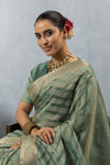 A close-up seated portrait of the model in a Vanya Sarees green Banarasi saree, showing the rich texture and designer blouse.