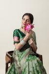 An elegant seated pose of the model in a Vanya Sarees green Banarasi silk saree, showcasing the hand-embroidered lotus on the blouse sleeve.