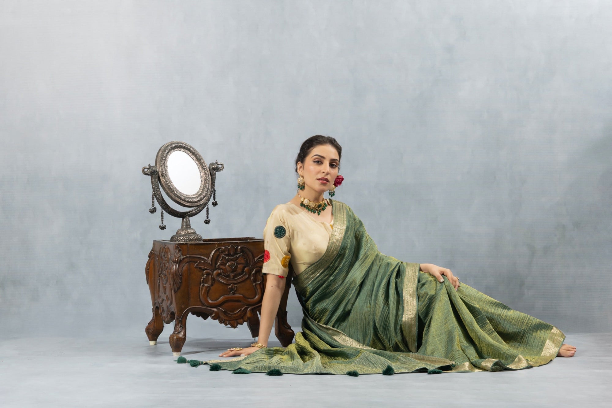Model seated gracefully on the floor in the Vanya Sarees green tissue silk saree, with the full ensemble beautifully displayed.