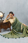 A romantic seated pose of the model resting by a vintage mirror, wearing the Vanya Sarees green saree and designer appliqué blouse.