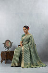 Model seated gracefully in the Vanya Sarees green Leheriya weave Banarasi saree, exuding timeless elegance.
