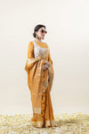 Full-length side profile of the model in the Vanya Sarees mustard yellow tissue silk saree, displaying the saree's tassels and rich drape.