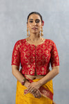 A clear front view of the Vanya Sarees readymade designer blouse in red Banarasi brocade with a gold zari floral pattern.