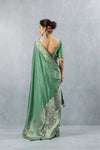 Full back view of the model in a Vanya Sarees sage green saree, showcasing the deep back blouse design and the drape of the floral woven pallu.