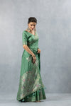 Graceful full-length side view of a model wearing the Vanya Sarees sage green designer saree, displaying the beautiful fall of the fabric and the rich pallu.
