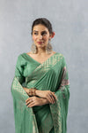 Close-up of the model in a Vanya Sarees sage green saree, highlighting the modern geometric gold zari border and the lustrous silk fabric.