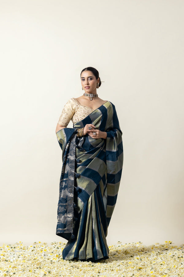 An elegant pose of the model in the Vanya Sarees teal blue striped Banarasi saree with its contrasting heavy embroidered blouse.