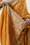 A detailed view of the intricate Banarasi-style woven zari border and tassels on the Vanya Sarees mustard yellow tissue silk saree.